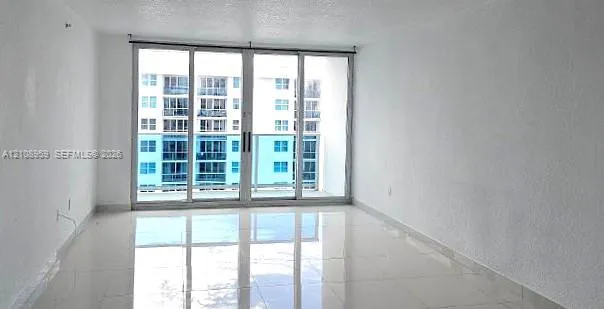 Interior space featuring large-format ceramic tile flooring, neutral wall finishes, and floor-to-ceiling sliding glass doors opening to a balcony