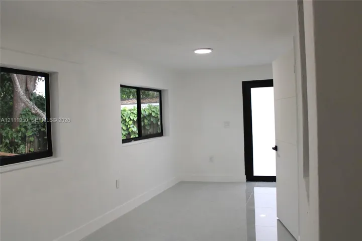 Interior space featuring neutral white walls, large-format tile flooring, recessed ceiling lighting, black-framed windows, and a modern door with black hardware