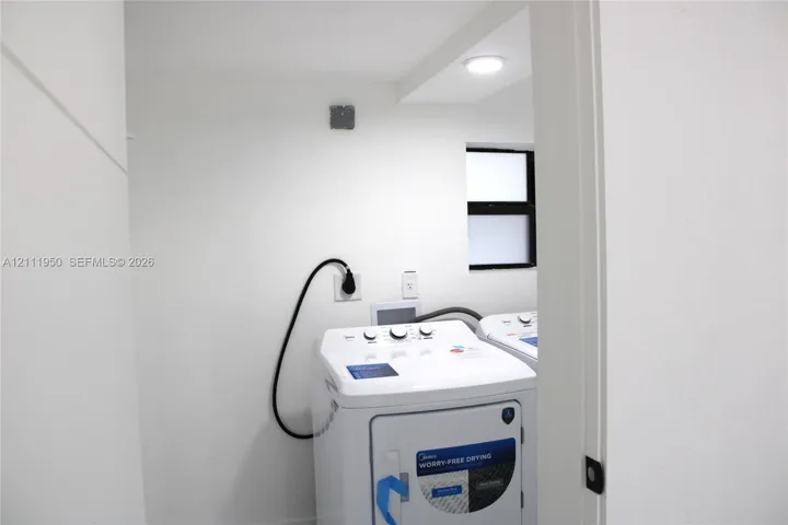 Laundry area featuring high-efficiency top-load washer, dedicated dryer hookups, recessed ceiling lighting, and a window