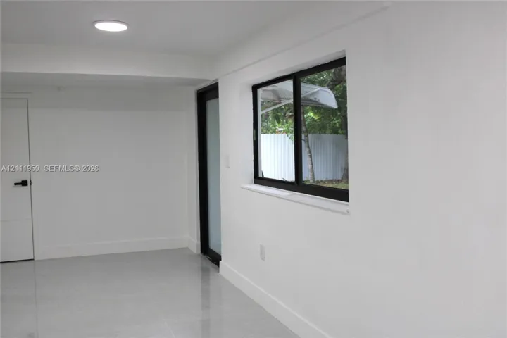 Neutral interior space featuring polished tile flooring, smooth white walls, recessed ceiling lighting, a dark-framed sliding window, and a frosted glass door with black hardware