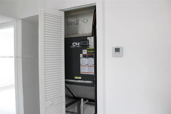 HVAC closet featuring a louvered bi-fold door, interior air handling unit, and wall-mounted digital thermostat