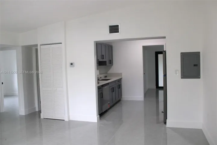 Kitchen featuring charcoal-toned cabinetry, light-toned countertops, and built-in dishwasher, accompanied by light-reflective flooring and louvered-panel closet doors