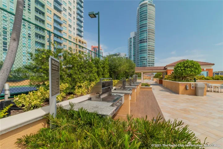 Outdoor grilling area featuring stainless steel built-in barbecue grills, stone-finish countertops, tile flooring, and mature landscaping