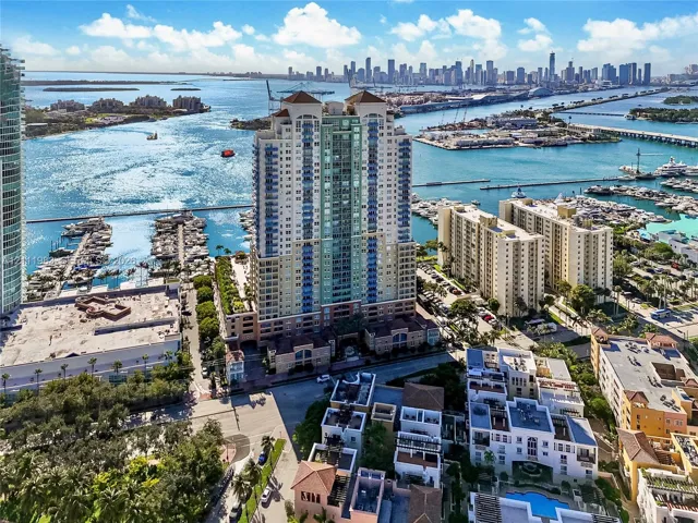 High-rise waterfront building featuring an expansive terrace deck, prominent architectural balconies, and proximity to a marina, set against a coastal skyline backdrop