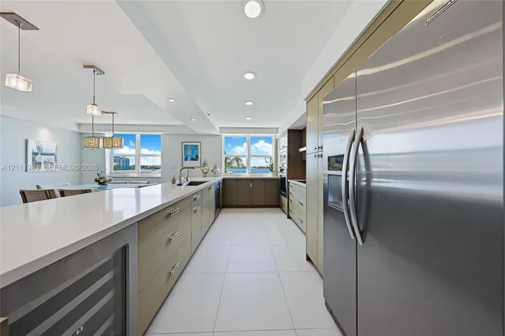 Kitchen featuring stainless steel appliances, flat-panel cabinetry, a long island with a solid-surface countertop, tile flooring, and integrated wine refrigeration