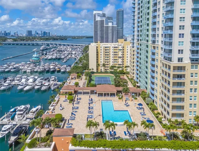 Outdoor recreational area featuring a paved pool deck, swimming pool, and tennis court, situated directly on a deep-water marina