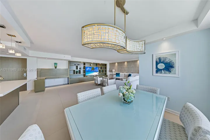 Open-concept space featuring large-format tile flooring, a custom built-in media wall, recessed ceiling lighting, and an ornate, multi-tiered metal and glass pendant light fixture