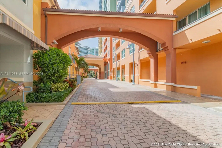 Paver-stone motor court featuring architectural archways, stucco exterior walls, and manicured perimeter landscaping