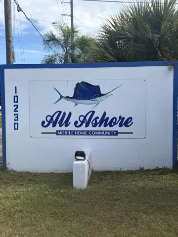 Stucco-finished community monument sign featuring blue-trimmed borders and integrated ground-mounted landscape lighting