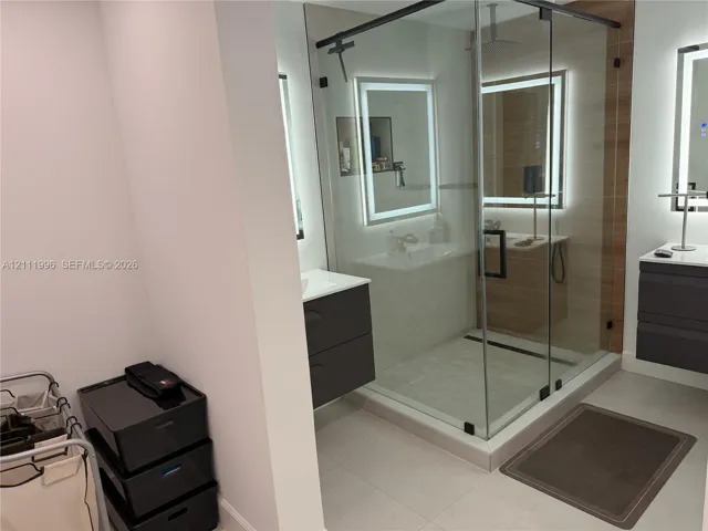 Glass-enclosed walk-in shower with a linear floor drain, floating charcoal vanities, dual LED-backlit mirrors, and tile flooring