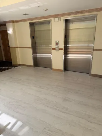 Common area elevator lobby featuring dual stainless steel elevator doors, large-format tile flooring, wood chair rail molding, and wall-mounted sconce lighting
