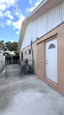 Exterior wall featuring stucco finish, vertical board siding, a white single-panel door with arched glass insert, and a concrete patio enclosure with chain-link fencing