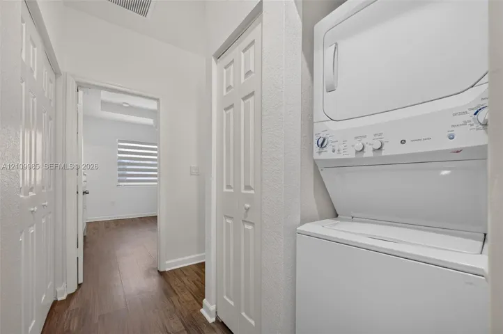 Dedicated laundry area featuring a stacked white washer and dryer unit, wood-finish flooring, and dual-panel closet doors