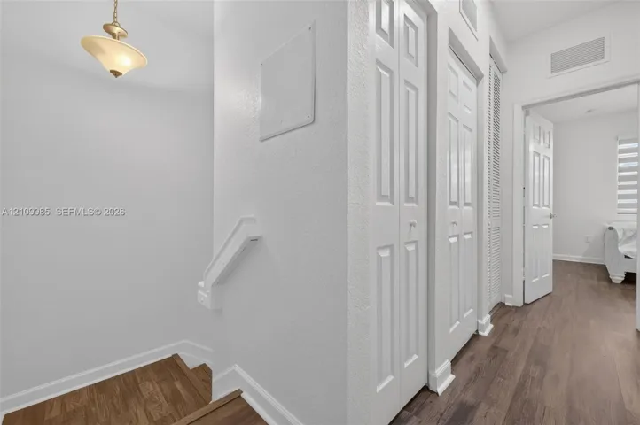 Hallway featuring wood-finish flooring, white panel doors, louvered closet doors, and a suspended pendant light fixture