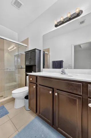 Bathroom featuring a dark wood vanity with white countertop, integrated sink, oversized wall-mounted mirror, glass-enclosed shower, and four-bulb vanity lighting
