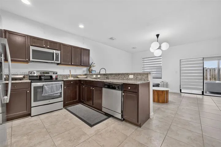 Kitchen featuring dark wood-finish cabinetry, stone-style countertops, stainless steel appliances, a modern multi-globe chandelier, and neutral floor tiling