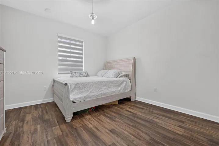 Interior room featuring wood-finish flooring, neutral wall paint, and a window equipped with dual-layered light-filtering shades