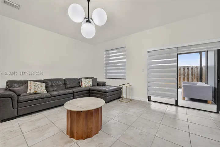 Neutral tile flooring, modern multi-globe chandelier, and sliding glass door with dual-tone horizontal roller shades