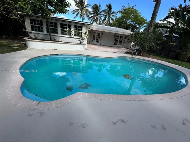 In-ground swimming pool with brick-style coping, concrete patio, white exterior walls, and dual sets of French doors