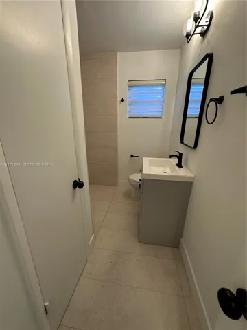 Bathroom featuring large-format neutral tile flooring, a modern grey vanity with a white rectangular sink, matte black hardware, and a framed vanity mirror
