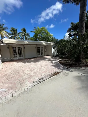 Rear patio featuring decorative concrete pavers, dual sets of French doors, an attached retractable awning, and mature palm landscaping
