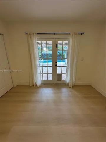 Interior space featuring wood-finish flooring, light-toned walls, and French doors leading to an exterior paved area with a swimming pool
