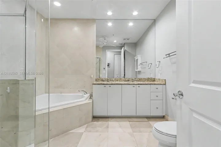 Main Bathroom featuring a double-sink vanity with stone countertop, corner soaking tub with tile surround, glass-enclosed shower, and large wall-mounted mirror
