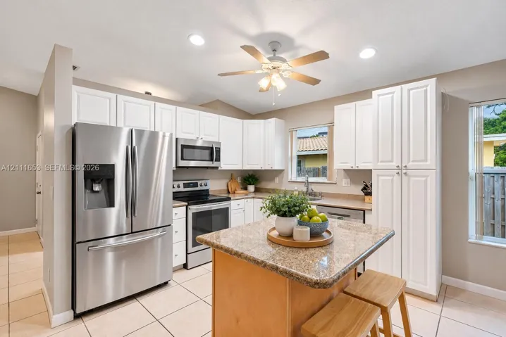 Kitchen featuring white cabinetry, stone-finish countertops, stainless steel appliances, a center island, and ceramic tile flooring