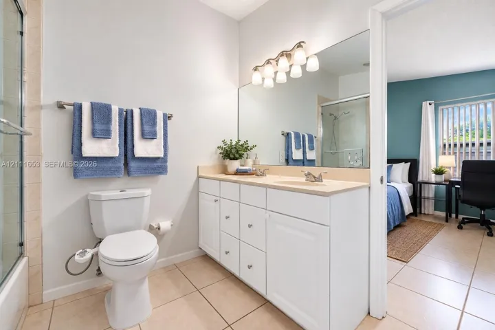 Primary Bathroom featuring white cabinetry, solid-surface vanity countertop with dual integrated sinks, full-width wall mirror, and tile flooring