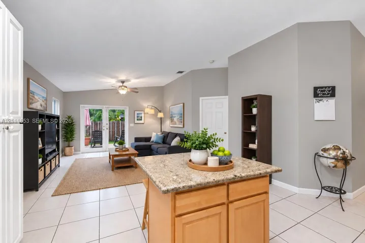 Kitchen island featuring a stone-composite countertop and natural-finish cabinetry, complemented by light-toned floor tile and French doors with integrated glass panels