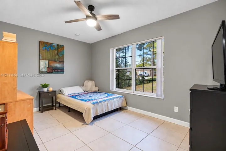 Bedroom 3 Neutral-toned walls featuring large-format ceramic tile flooring, a multi-pane window with grid detailing, and a modern ceiling fan with integrated lighting