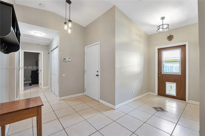 Foyer featuring ceramic tile flooring, vaulted ceilings, multi-light pendant lighting, a glass-panel entry door, and a built-in wall shelf