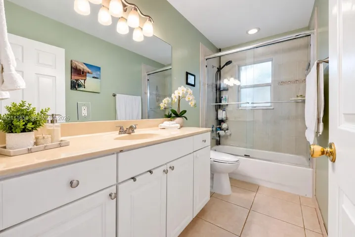 Guest Bathroom featuring white cabinetry, integrated sink, large wall-mounted mirror, ceramic tile flooring, and a shower-tub combination with glass enclosure