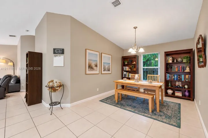 Neutral-toned interior featuring ceramic tile flooring, vaulted ceilings, and a decorative multi-arm chandelier