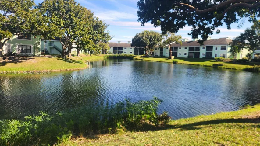 Expansive central pond bordered by manicured lawn, mature trees, and multi-story residential structures