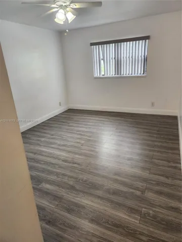 Room featuring wood-finish flooring, a ceiling fan with integrated lighting, and a window with fitted blinds