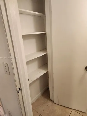 Built-in storage closet featuring painted white shelving and tile flooring