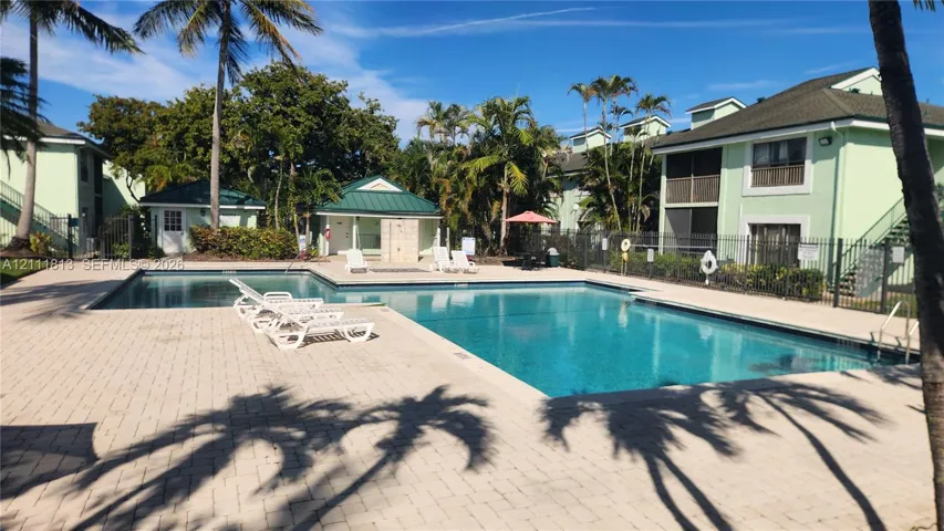 Outdoor swimming pool featuring a brick-paver deck, perimeter metal fencing, and mature palm trees