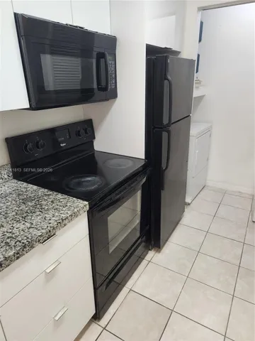 Kitchen featuring white flat-panel cabinetry, stone-patterned countertops, black appliances, and ceramic tile flooring