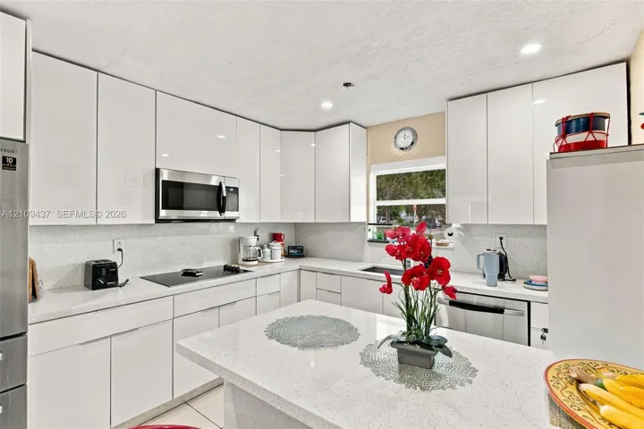 Kitchen featuring white gloss cabinetry, stone-finish countertops, stainless steel built-in appliances, recessed lighting, and an island