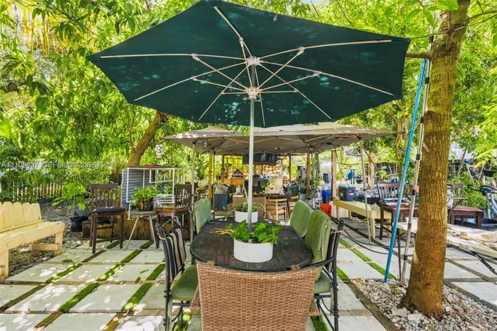 Outdoor patio area featuring a grid-pattern paver surface with integrated ground cover, mature canopy trees, and a wooden bench