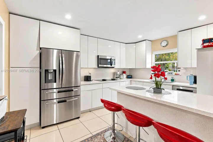 Kitchen featuring high-gloss white cabinetry, solid surface countertops, stainless steel appliances, recessed lighting, and tile flooring