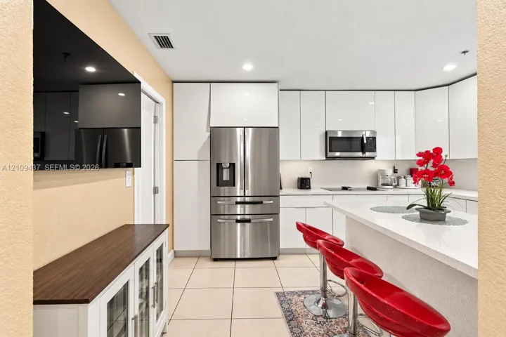 Kitchen featuring white high-gloss cabinetry, stainless steel appliances, quartz countertops, a kitchen island, and ceramic tile flooring