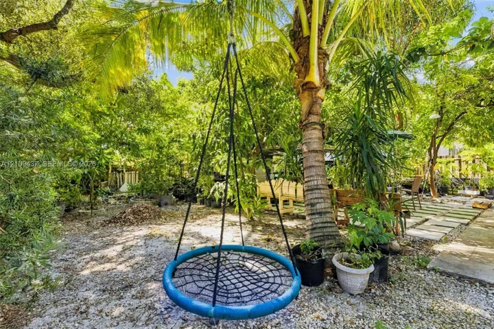 Backyard featuring mature palm trees, dense tropical landscaping, stone paver pathway, and crushed stone ground cover