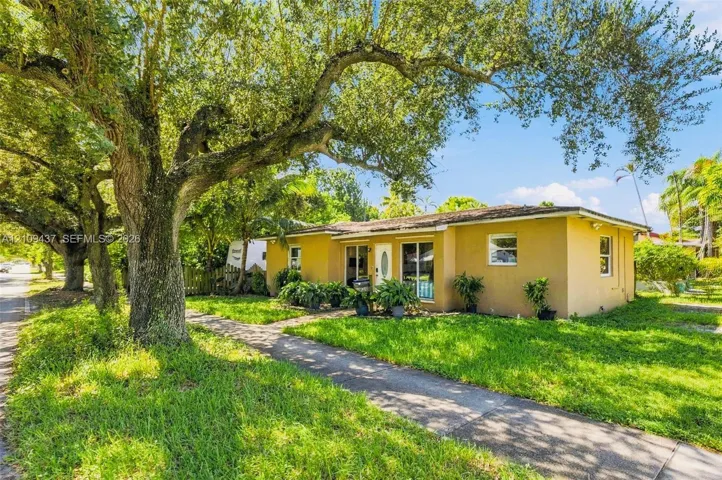 Stucco exterior residence featuring mature oak trees, a concrete walkway, and expansive green space