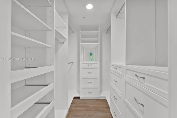 Walk-in closet featuring white built-in cabinetry, custom shelving, integrated dresser drawers, chrome hardware, and wood-finish flooring