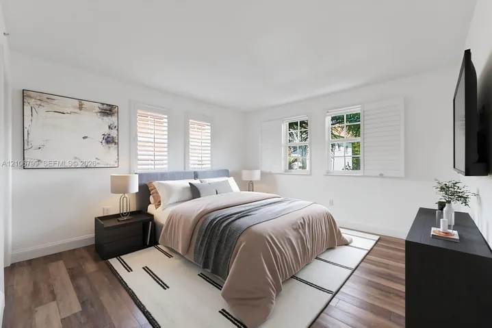 Bedroom featuring wood-finish flooring, white walls, and multi-pane windows equipped with adjustable plantation shutters