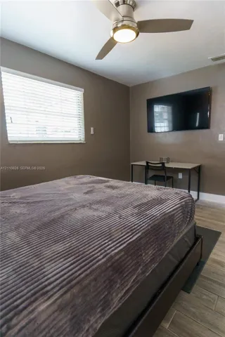 Interior space featuring wood-finish flooring, neutral wall tones, a ceiling fan with integrated light fixture, and horizontal window blinds