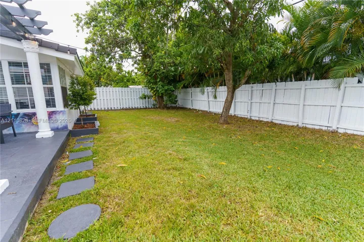 Backyard featuring a white vinyl privacy fence, pergola-covered patio, paved stone walkway, and mature landscaping