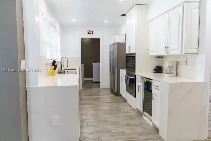 Kitchen featuring white cabinetry, quartz countertops with waterfall edge, wood-finish flooring, stainless steel wall-mounted oven, and recessed lighting